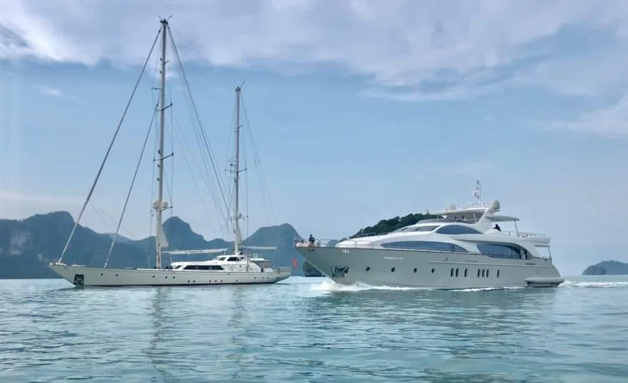 Sailing yacht and motor yacht on flat water off a steep wooded coastline